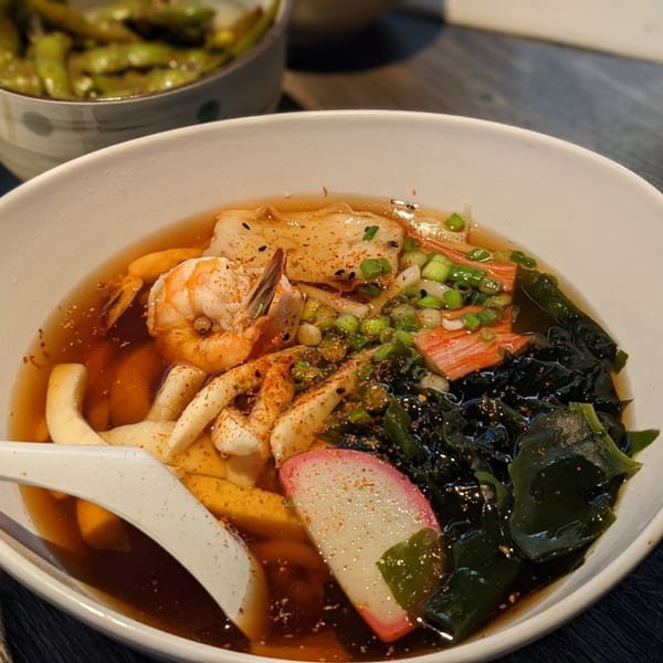 A bowl of Japanese udon soup with shrimp, squid, fish cake, seaweed, and scallions.